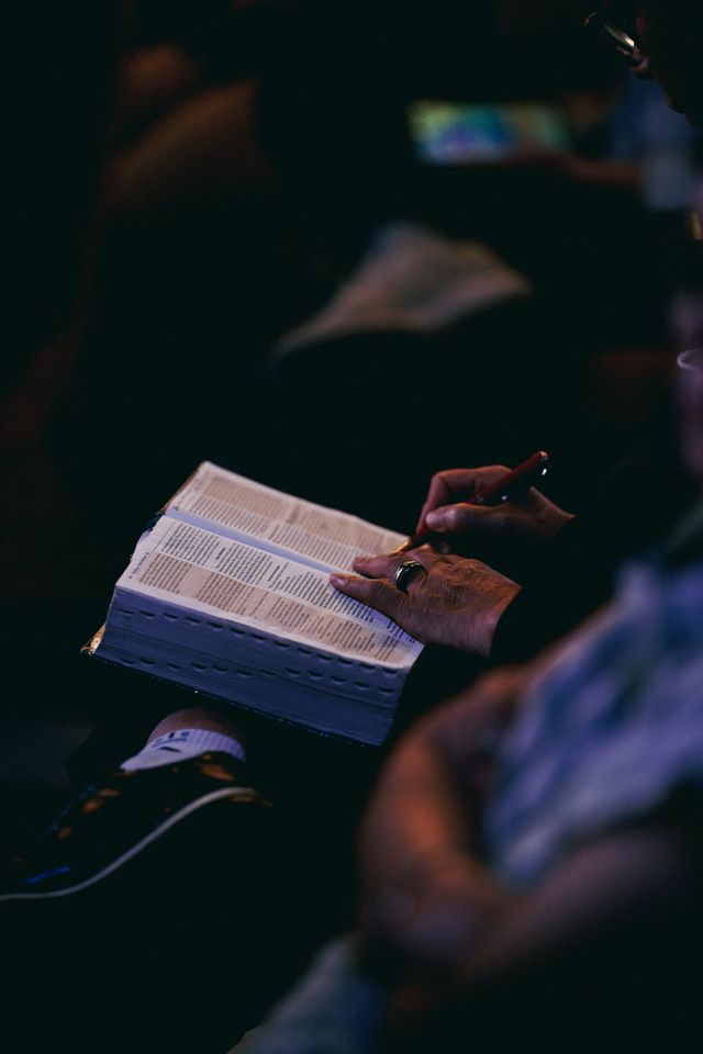 A woman reading a Bible, focusing in a dimly lit room, conveying a sense of contemplation.